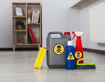 Bottles of toxic household chemicals with warning signs, brush and scouring sponge in room, space for text